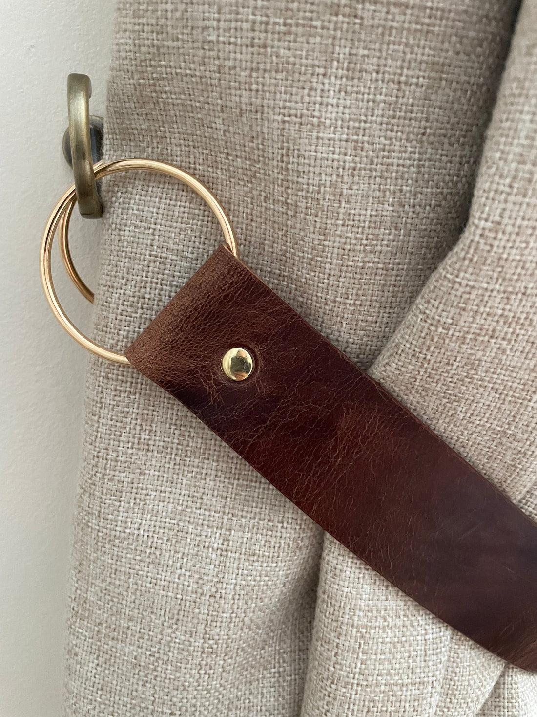 Handmade leather curtain tie-backs styled in a living room — natural, black, antique brown, red and yellow colourways shown