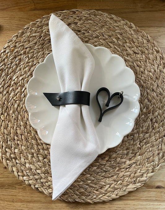 Black leather napkin ring with side stud fastening around a white napkin on a white plate